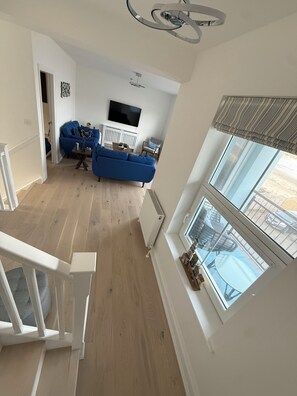 A spacious living room with a blue sofa, a white fireplace, and a large window with a view of the outdoors.