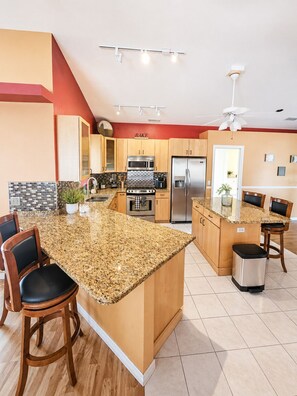 A modern kitchen with granite countertops, stainless steel appliances, and wooden cabinetry. - Cape Coral Retreat w Pool & Court (Cape Coral)