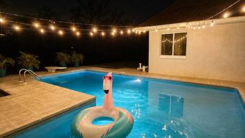 Une piscine avec un flotteur en forme de flamant rose, des guirlandes lumineuses et des plantes en pot.