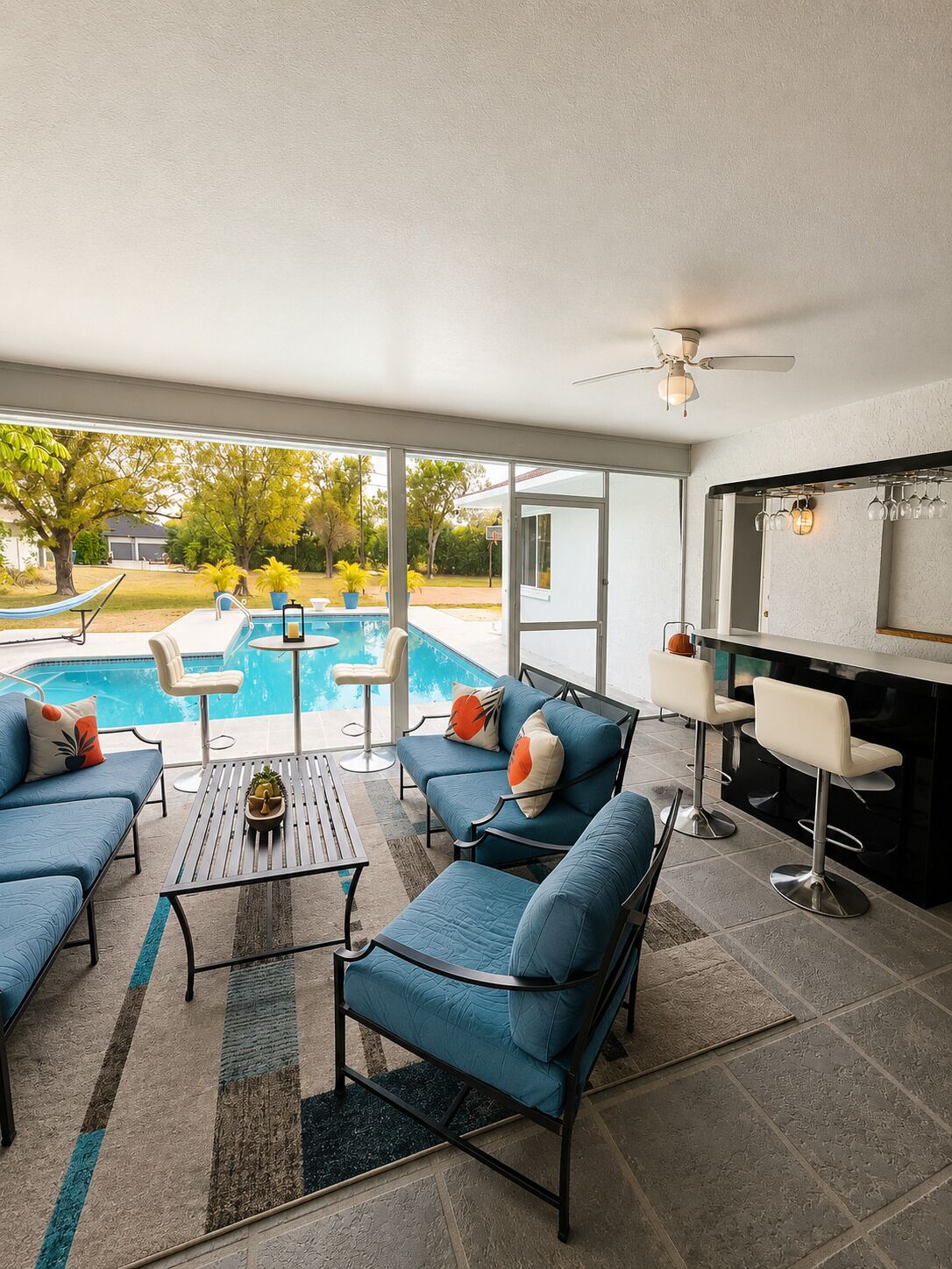 Zona junto a la piscina con mobiliario exterior, ventilador de techo y área de bar con vasos.