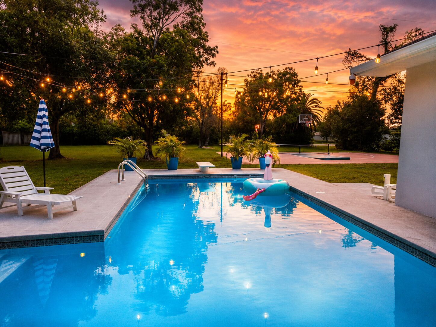 A swimming pool with a lounge chair and a small inflatable pool float, surrounded by trees and string lights.