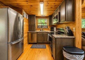 A compact kitchen with wooden cabinets, stainless steel appliances, and a 'LIVE LARGE' sign. - Relax by the Waterfall ,Hot Tub,Pet-Friendly (Sevierville)