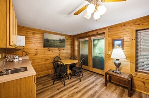 A wooden interior with a dining table, chairs, a ceiling fan, a window with blinds, and a small table with a lamp. - Relax by the Waterfall*Hot Tub*Pet-Friendly (Sevierville)