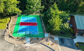 Uma quadra de tênis cercada por árvores e um edifício com telhado verde.