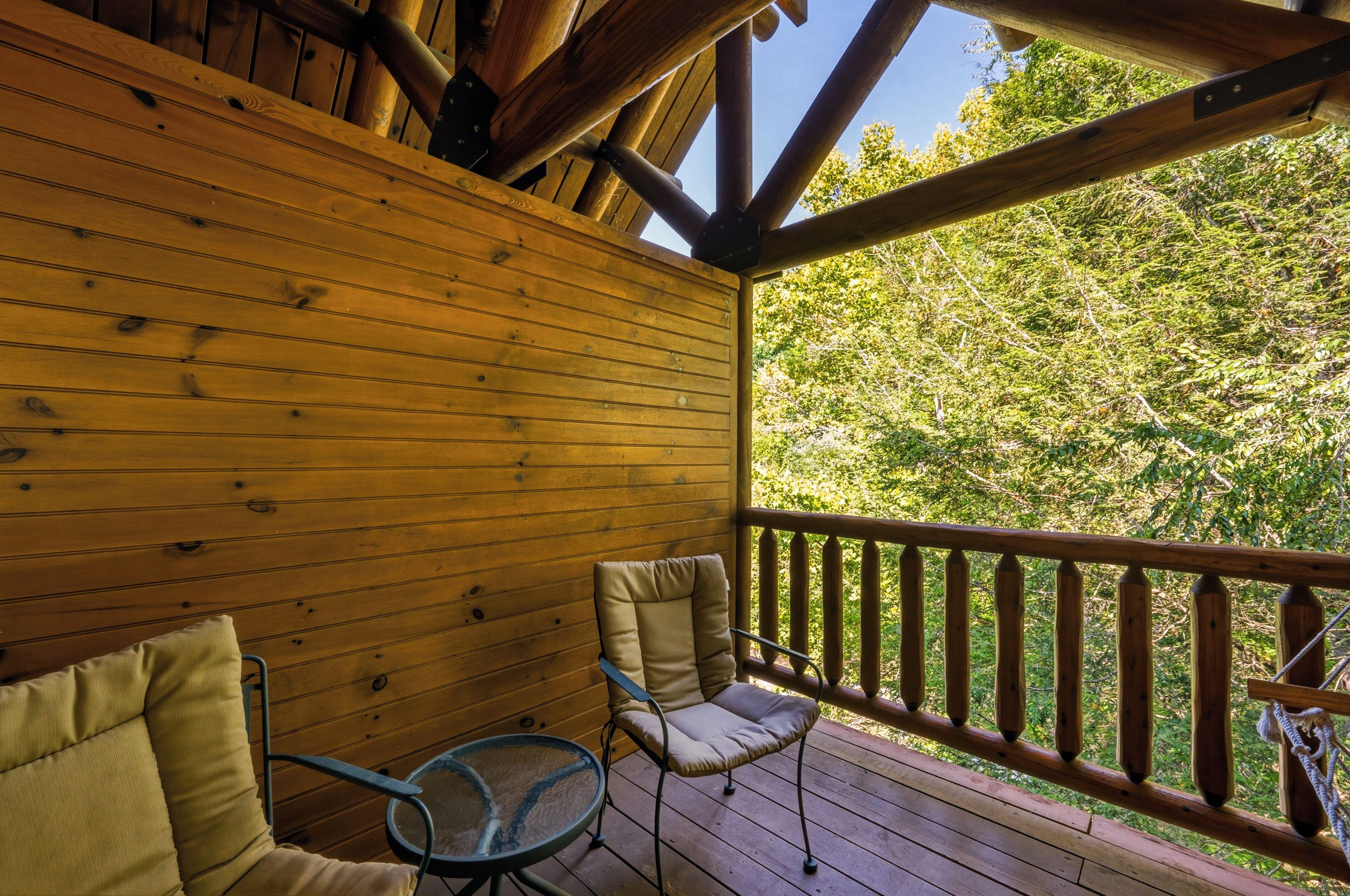 A wooden deck with a view of a forest, two chairs, and a table.