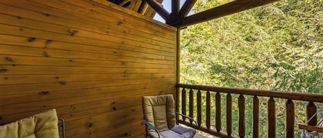 A wooden deck with a view of a forest, two chairs, and a table.
