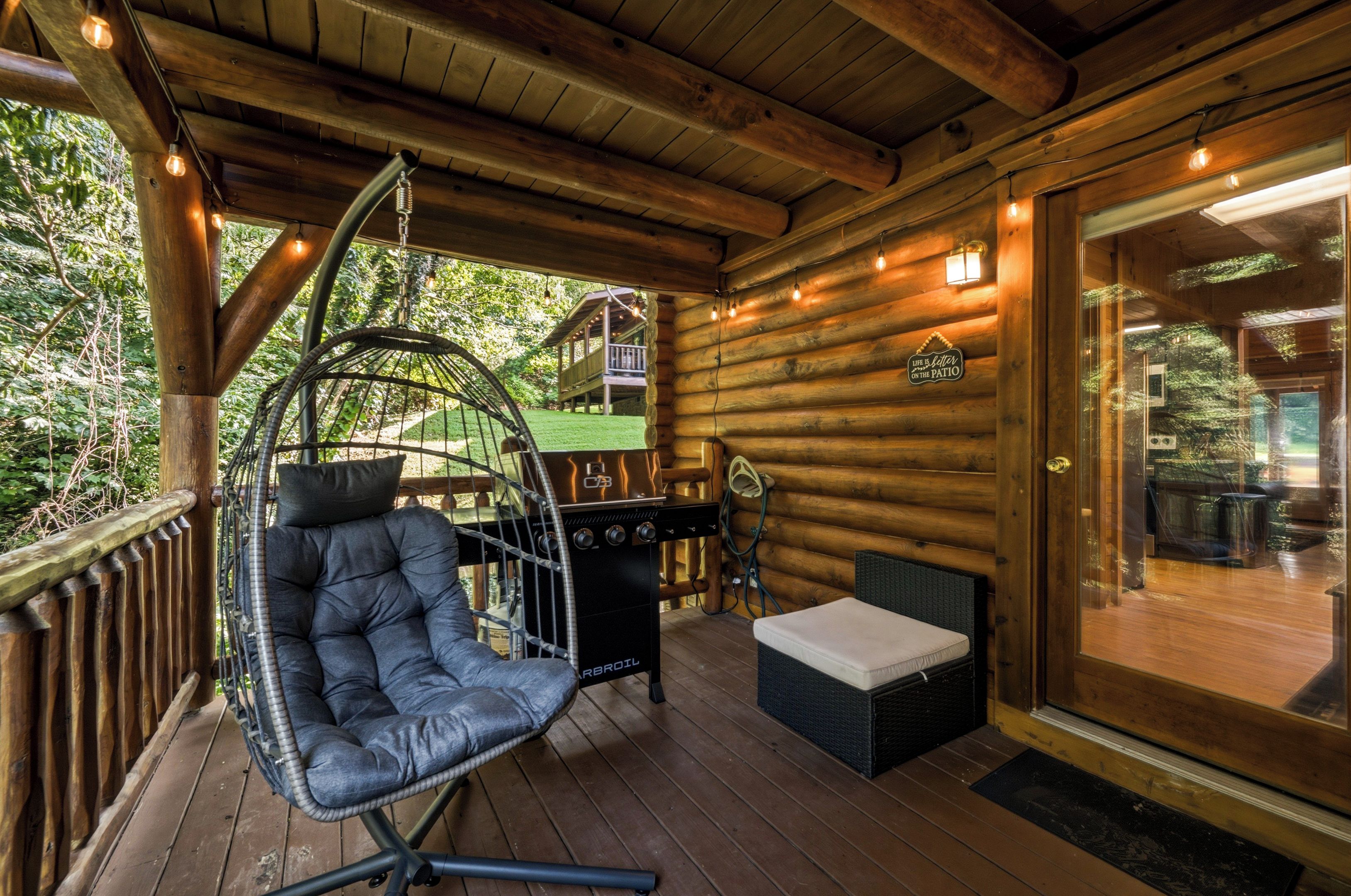 Een houten terras met een hangstoel, een barbecue en een glazen deur die uitkomt op een buitenruimte.