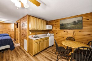 A compact room with a kitchenette, a dining area with chairs, a bed with a blue cover, and a painting on the wall. - Relax by the Waterfall*Hot Tub*Pet-Friendly (Sevierville)