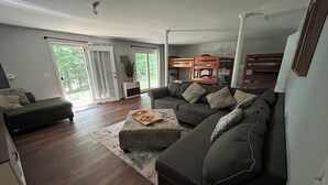 A modern living room with a sectional sofa, a small ottoman, and a large window with curtains.