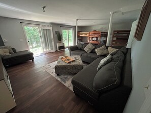 A modern living room with a sectional sofa, a small ottoman, and a large window with curtains.