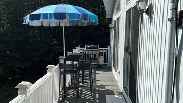 A covered outdoor deck with a table and chairs, a blue umbrella, and a barbecue grill.