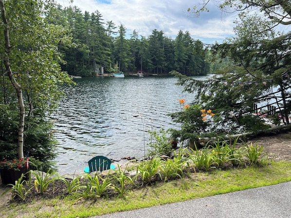 A lakeside view with a dock, greenery, and a chair by the water.