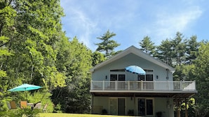 A two-story house with a balcony, surrounded by a grassy yard and trees.