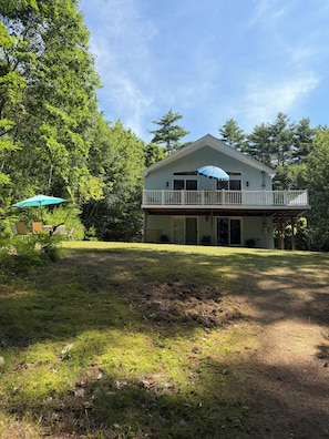 A two-story house with a balcony, surrounded by a grassy yard and trees.