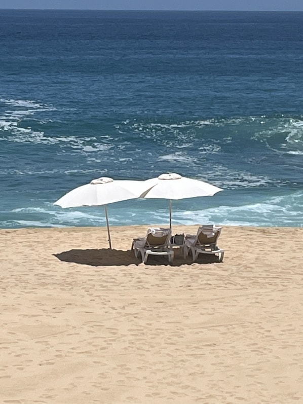 A beach with two white umbrellas and two lounge chairs facing the ocean.