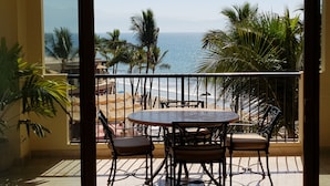 A balcony with a table and chairs, overlooking a beach with palm trees and the ocean. - Luxury Two Bedroom Ocean Front Penthouse with Spa on Terrace at Villa del Palmar (Loreto)