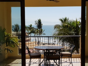 Een balkon met een tafel en stoelen, met uitzicht op een strand met palmbomen en de oceaan.