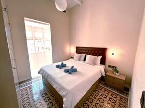 A neatly made bed with a headboard, a bedside table with a lamp, and a patterned floor. - Serene 1-bedroom apartment with AC in Il-Belt Valletta (Il-Belt Valletta)