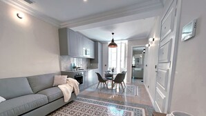 Une cuisine moderne avec des meubles gris, un coin repas avec une table et des chaises, et un canapé gris agrémenté d’un plaid.
