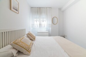 A bedroom with a bed, a window with curtains, a radiator, and a wall-mounted mirror. - Home2Book Sevilla Terrace & Pool Apt (Seville)