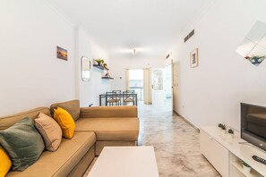A modern living room with a sofa, a coffee table, a TV, and a dining area with chairs and a table. - Home2Book Sevilla Terrace & Pool Apt (Seville)