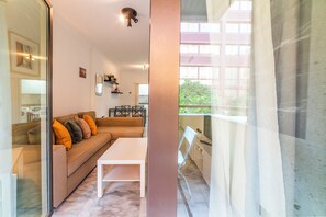 A modern living room with a sofa, a small table, and a balcony with a view. - Home2Book Sevilla Terrace & Pool Apt (Seville)