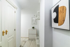 A hallway with a white door, a small white cabinet with a plant, and a framed map on the wall. - Home2Book Sevilla Terrace & Pool Apt (Seville)