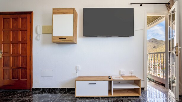 Quarto com porta de madeira, telefone fixo, televisão e aparador de madeira com uma gaveta.