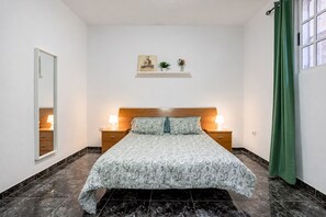 A bedroom with a bed, two bedside tables, a nightstand, a mirror, a wall-mounted shelf with decorative items, and a green curtain. - Home2Book Ocean & Mountain View in San Andrés (San Andres de Tenerife)