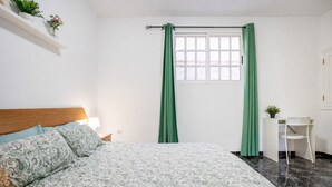 Quarto com cama, escrivaninha e janela com cortinas verdes.