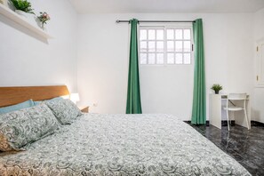 Ein Schlafzimmer mit einem Bett, einem Schreibtisch und einem Fenster mit grünen Vorhängen.