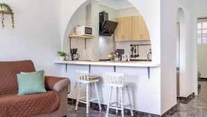 Um espaço compacto com cozinha compacta, um sofá marrom com almofada verde e uma cadeira branca.