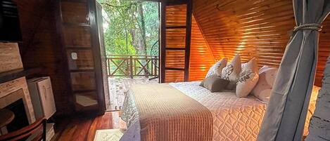 Un dormitorio de cabaña de madera con cama, mesita de noche y vistas al exterior.