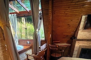 A wooden interior with a fireplace, a dining table, and a window with curtains. - VELINN Pousada Canto da Cascata (Monte Verde)