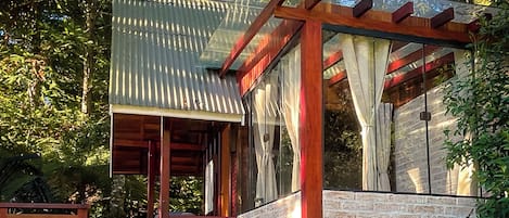 A wooden pergola with a corrugated metal roof, a stone wall, and a glass door.