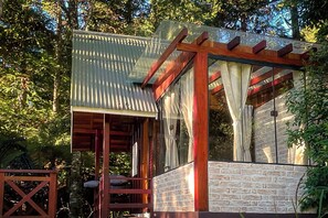 A wooden pergola with a corrugated metal roof, a stone wall, and a glass door.