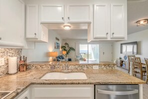 A kitchen with white cabinets, a granite countertop, and a view to the living area. - Luxury Oceanfront Carolina Beach Condo w/ Private Beach Access. Full ocean view! (Carolina Beach)