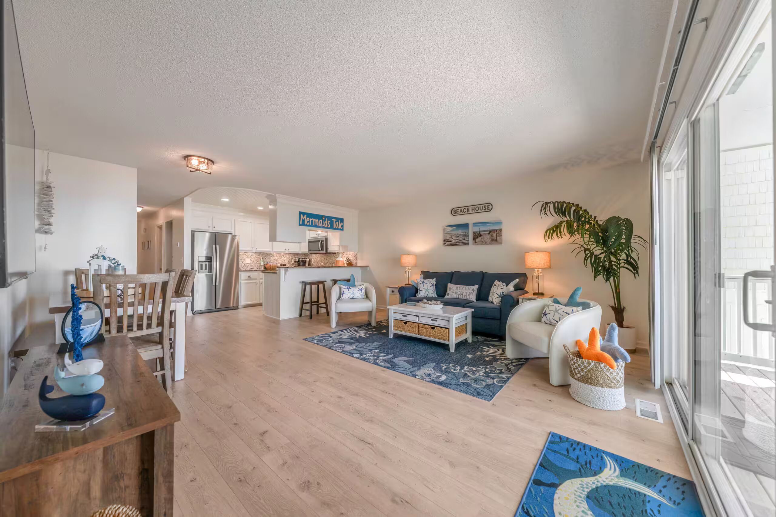 A spacious living area with a kitchen in the background, a dining table with chairs, and a large window providing natural light.