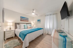 Une chambre à coucher avec un lit, des tables de chevet, un ventilateur de plafond, une télévision et une fenêtre avec des rideaux.