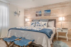 Ein Schlafzimmer mit Holzpaneelen, einem Bett mit blauer und weißer Bettdecke, zwei Nachttischlampen und einer kleinen Ablage mit Dekoration.