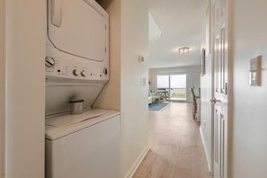 Une buanderie équipée d’un lave-linge et d’un sèche-linge, un couloir menant à un balcon avec vue, et une porte dotée d’un interrupteur.