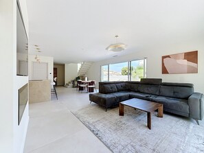 A modern living room with a sectional sofa, a coffee table, and a dining area with chairs. - Villa Neuve avec Jardin Tropical à 700m de la mer (AGDE)