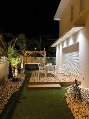 Eine Terrasse mit Holzdeck, weißen Stühlen und einem Tisch.
