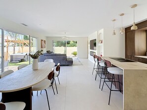 A modern kitchen with a dining area, large windows, and a sliding glass door leading to a patio. - Villa Neuve avec Jardin Tropical à 700m de la mer (AGDE)