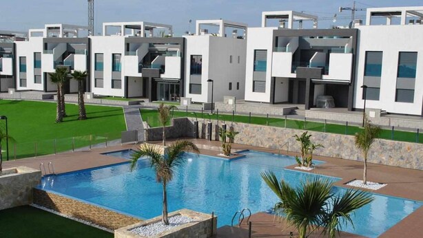 A modern hotel with a large rectangular pool surrounded by palm trees and a well-maintained lawn. - Groundfloor Oasis Beach VII Punta Prima (Torrevieja)
