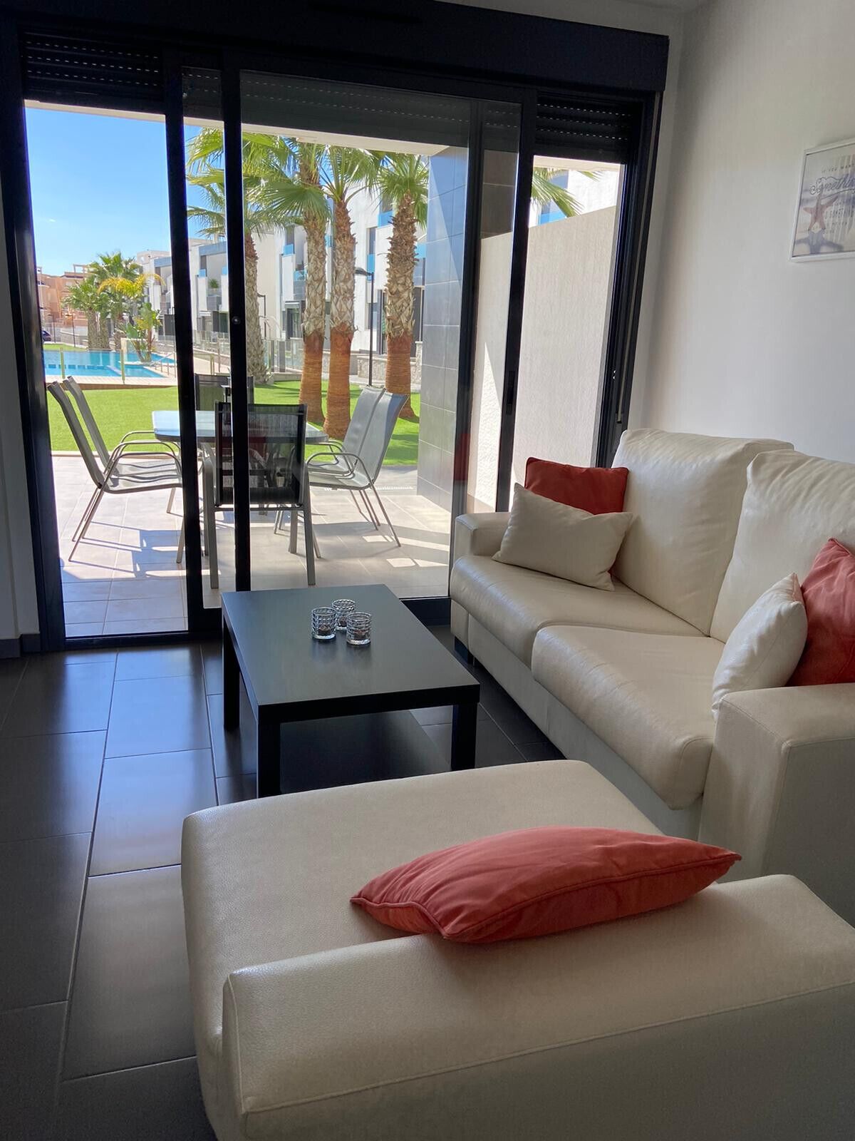 A modern living room with a sofa, a coffee table, and a view of a pool and palm trees through large glass doors.