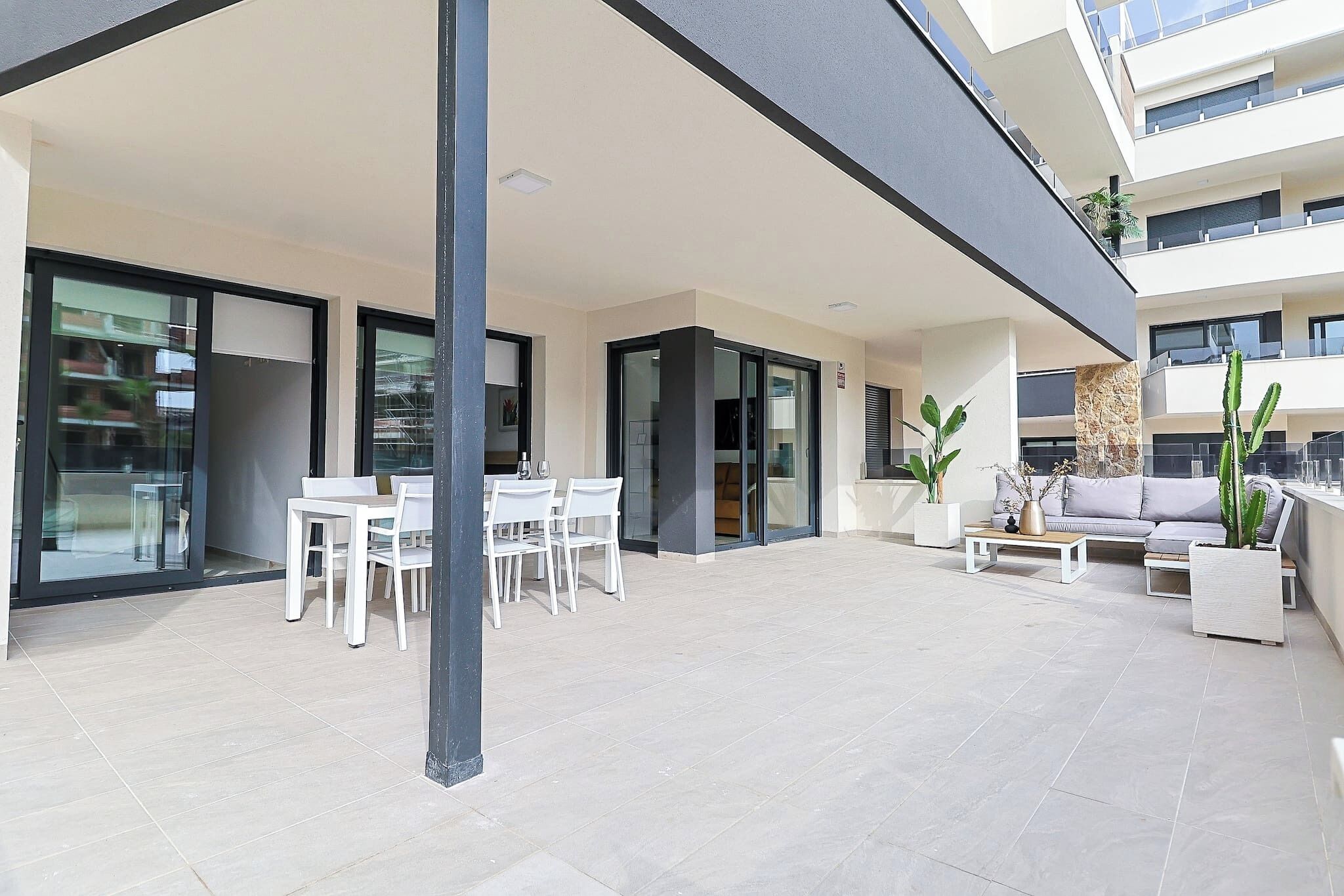 A modern outdoor patio area with a dining table and chairs, a sofa, and potted plants.