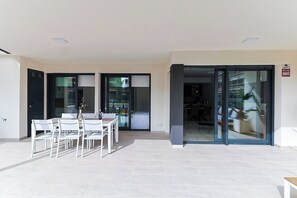 A modern outdoor patio with a dining table and chairs, a sliding glass door leading to an interior space, and a tiled floor. - Groundfloor Villamartin Amanecer (Orihuela)
