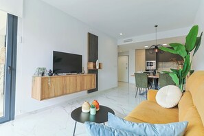 Ein modernes Wohnzimmer mit Flachbildfernseher, Holzschrank, Essbereich und einer großen Pflanze.