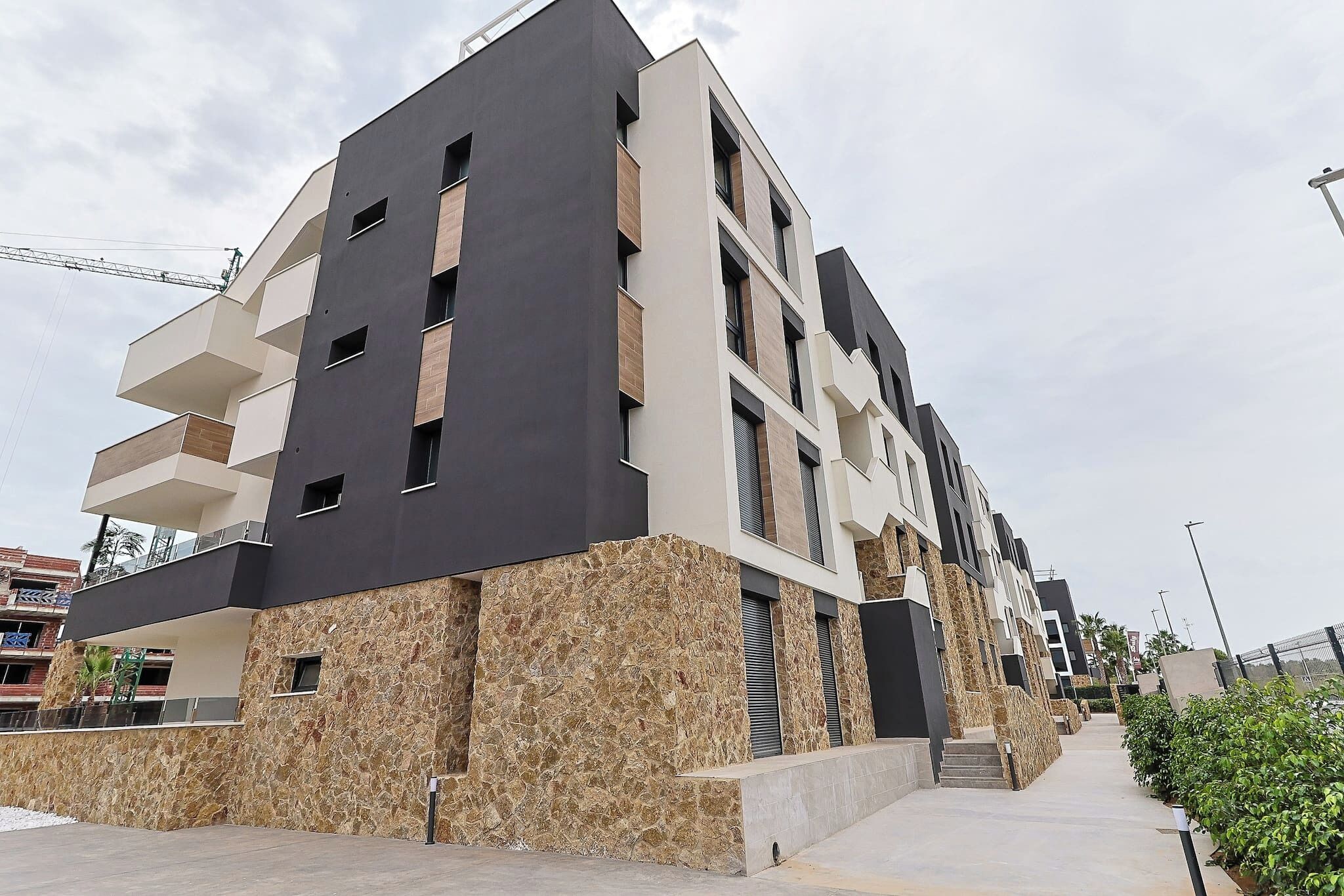 A modern multi-story building with balconies, a stone facade, and a clear sky.